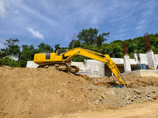 A large yellow excavator is currently positioned on top of a huge pile of dirt