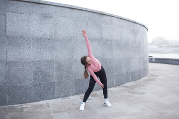 A sporty girl is dressed in sport clothes, leggins and rush guard doing sport exercises outside...