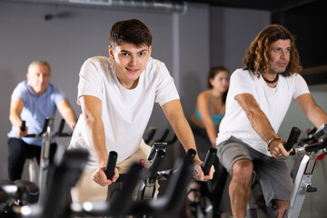 Portrait of concentrated young guy doing cardio training, cycling on stationary bike in gym. Sport...