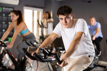 Focused sporty young guy working out on stationary bicycle in gym. Physical activity and fitness...