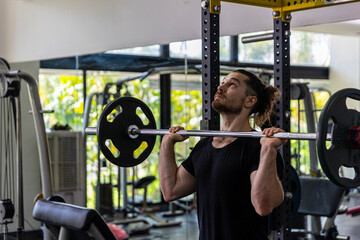 Good looking fitness trainer shows how to raise heavy barbell from squat racks with safety steps as part of body building exercise. A man using barbell to improve his physical power in a gym