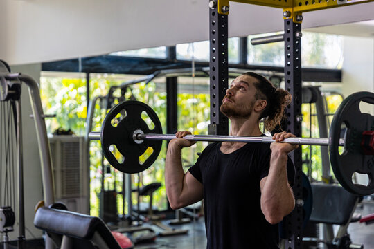 Good looking fitness trainer shows how to raise heavy barbell from squat racks with safety steps as part of body building exercise. A man using barbell to improve his physical power in a gym