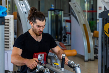 Young good looking physical trainer shows how to build upper part body by pulling up an equipment in a fitness room. A muscular sport man taking an exercise with fitness equipment to build his body.
