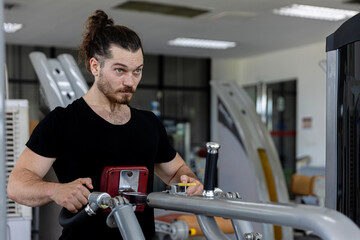 Young good looking physical trainer shows how to build upper part body by pulling up an equipment in a fitness room. A muscular sport man taking an exercise with fitness equipment to build his body.