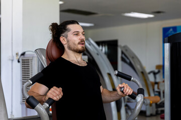 Young good looking physical trainer shows how to build upper part body by pulling up an equipment in a fitness room. A muscular sport man taking an exercise with fitness equipment to build his body.
