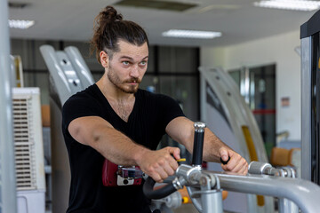 Young good looking physical trainer shows how to build upper part body by pulling up an equipment in a fitness room. A muscular sport man taking an exercise with fitness equipment to build his body.