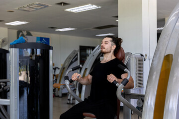 Young good looking physical trainer shows how to build upper part body by pulling up an equipment in a fitness room. A muscular sport man taking an exercise with fitness equipment to build his body.