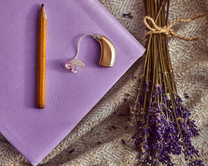 BTE hearing aid rests next to a pencil and dried lavender on soft textures, symbolizing care and...