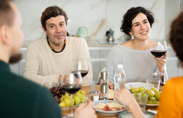 Group of joyful individuals are celebrating a holiday, enjoying drinks and conversation around a...