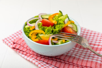 Cucumber salad on a wooden background.Homemade salad with fresh vegetables, cucumber, tomato, sweet pepper and lettuce in a plate.Vegetarian spring salad.Vegetarian diet.Healthy eating.Space for text
