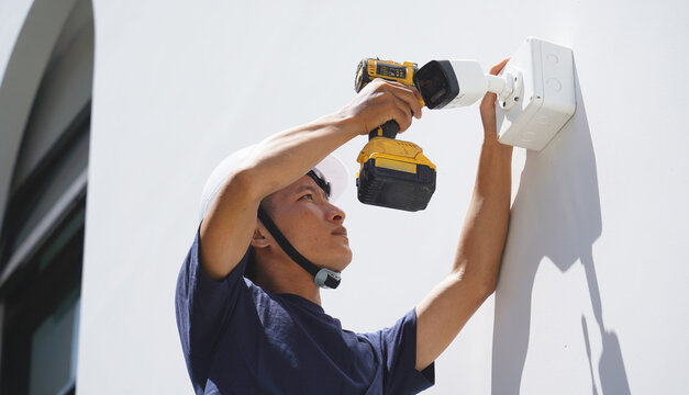 A technician installs a CCTV camera on the facade of a residential building