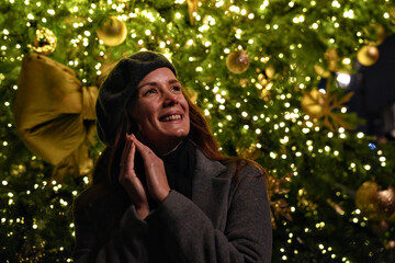 Brunette with long hair dressed in a gray coat and scarf in front of illuminated festive decorations