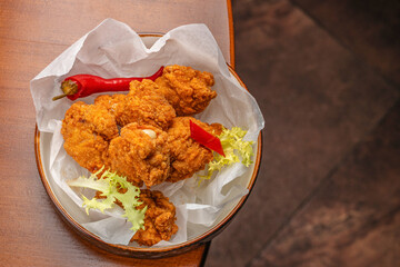 Crispy golden fried chicken pieces served in a bowl with chili pepper and fresh lettuce on...