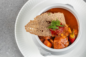 Rich and hearty meat stew with vegetables, served in a white bowl and topped with rye crispbread, spicy sauce, and fresh dill