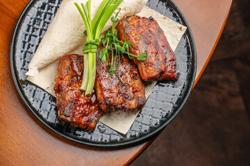 Barbecue pork ribs served with flatbread and green onion garnish on a black ceramic plate