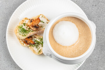 Creamy mushroom soup with a frothy top served alongside toasted baguette slices topped with sauteed mushrooms and fresh dill