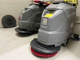 Two industrial floor scrubbers with brushes and an extra scrubbing pad, demonstrating heavy-duty cleaning equipment for large commercial and industrial spaces