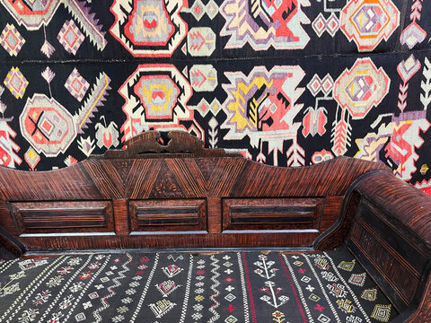 A vibrant Moldovan traditional rug with intricate geometric and stylized animal patterns displayed behind a stack of embroidered pillows and woven textiles, showcasing rich cultural decor