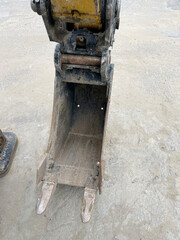 A close-up of a well-worn yellow excavator digging bucket with visible teeth, highlighting heavy-duty construction attachments for precise earthmoving and material handling