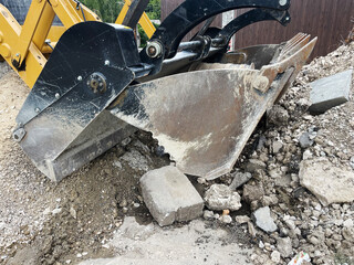 The rear digging bucket of a yellow backhoe loader, extended into a trench, illustrating heavy...