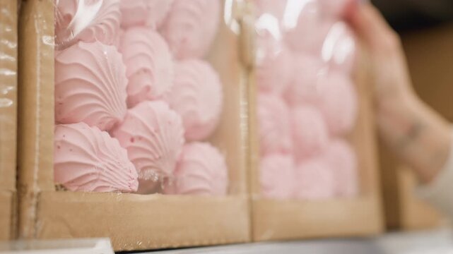 Close up view of shopper placing pink swirl cookie carton on grocery shelf, capturing hand motion and texture, supermarket aisle shows bakery display, packaged treats selection