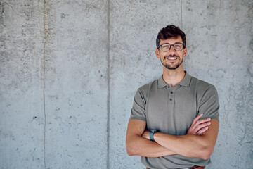 Fototapeta premium Portrait of a smiling businessman with crossed arms, exuding confidence and professionalism against a textured concrete wall