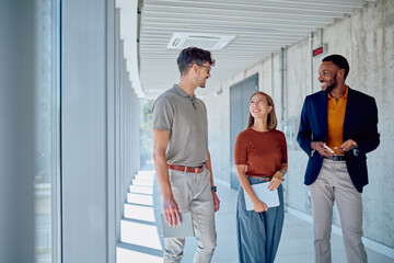 Three colleagues are walking through a modern office building, discussing work and collaborating on a project