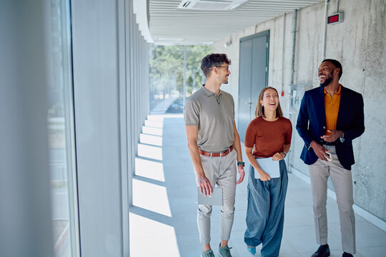 Multi-ethnic business team walking and chatting together in a bright, modern office corridor, fostering collaboration and connection