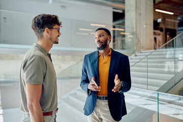 Two businessmen holding smartphones and discussing during a break in a modern office building...