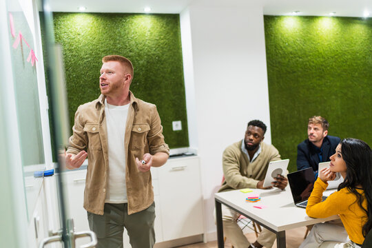 Young manager is leading a business meeting with his team, presenting a project in a modern coworking office with a green wall