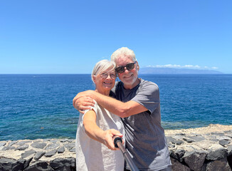 Smiling senior couple along sea coast get a selfie enjoying summer vacation expressing happiness...