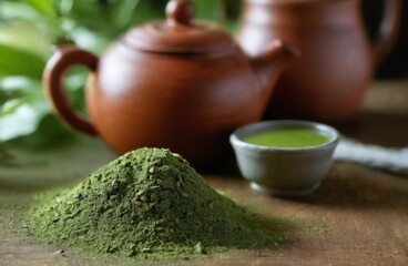 Closeup shot of clay teapot and matcha green tea powder on wooden table, surrounded by green leaves, creating a serene ambiance.