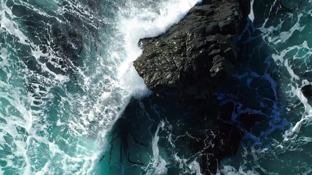 Aerial view of ocean waves crashing against rocks in Big Sur, California, USA. The turquoise water creates a dynamic scene of nature's power and beauty.