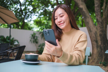 Portrait image of a woman holding and using mobile phone while drinking coffee in the outdoors cafe