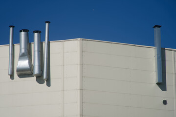 Low‑angle capture of silver ventilation stacks fixed to a paneled building facade under vivid...