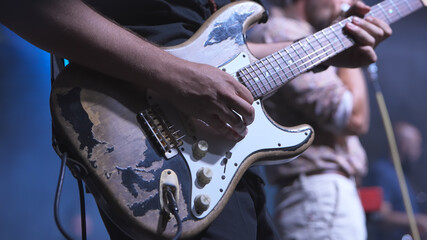Guitarist playing worn electric guitar on stage during concert