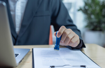 Businessman stamping approval on finance, banking, or investment marketing documents at desk. Concept of authorization, business validation, and official approval process.