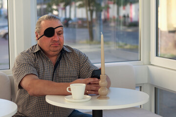 Man with eye patch using a smartphone in a cozy cafe setting