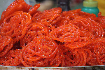 Crispy Indian sweet Jalebi, traditional golden spiral dessert, popular Diwali and Holi festival food, vegan sugary syrup snack on plate.