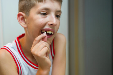 Litle caucasian boy holds a dropped milk tooth between his fingers with copy space