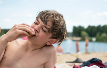 A little boy eats food on the beach after swimming