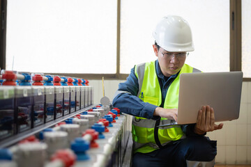 Engineer wearing safety helmet and vest performing inspection on battery system at electrical...