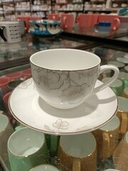 Elegant ceramic teacup with floral design displayed in store surrounded by colorful dishware