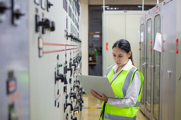 Engineer in power station control room uses laptop to monitor systems ensuring efficient operation...
