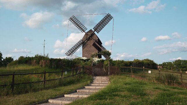 Historic German Wooden Windmill, Slow Rotating Blades on a Scenic Summer Landscape with Blue Sky and Clouds.