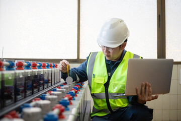 Engineer wearing safety helmet and vest performing battery inspection at stationary substation...