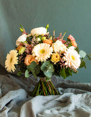Soft romantic still-life of pastel flower bouquet on textured linen cloth in warm naturally lit interior room
