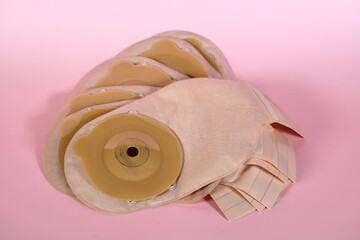 Medical ostomy bags with adhesive rings arranged on pink surface, showcasing hygienic stoma care...