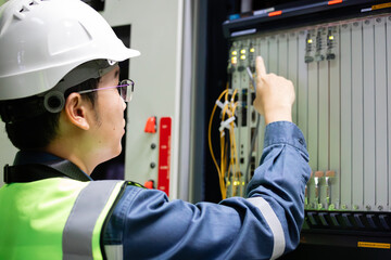 Network technician performing inspection on electronic control panel with focus and care in industrial environment