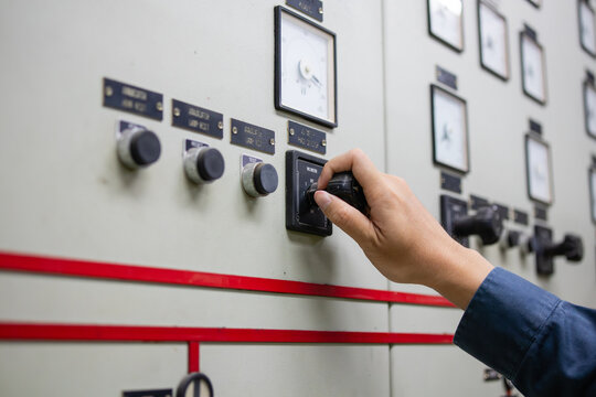 Power station control room engineer adjusting switch on electrical panel with meters and knobs in industrial environment